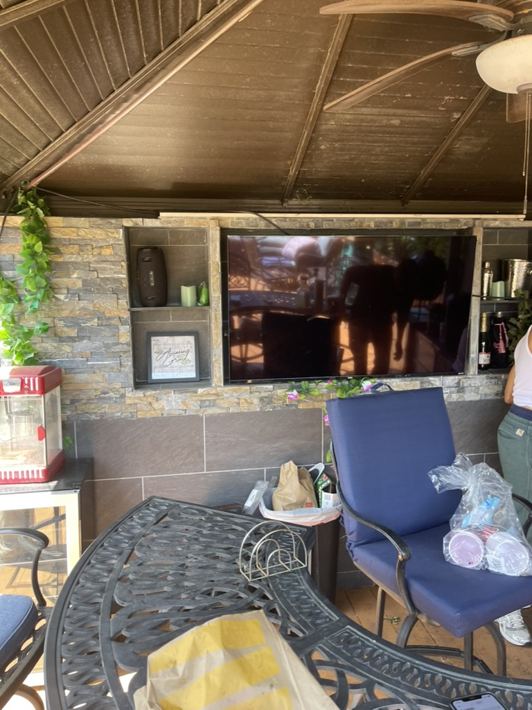 Covered patio lounge with mounted TV, speakers, and bar seating